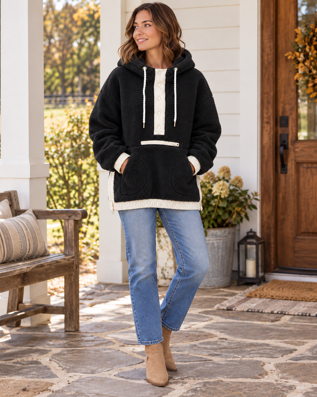 Woman wearing a black two-toned sherpa pullover hoodie with ivory trim, white rope drawstrings, and front pockets, styled with jeans and tan boots
