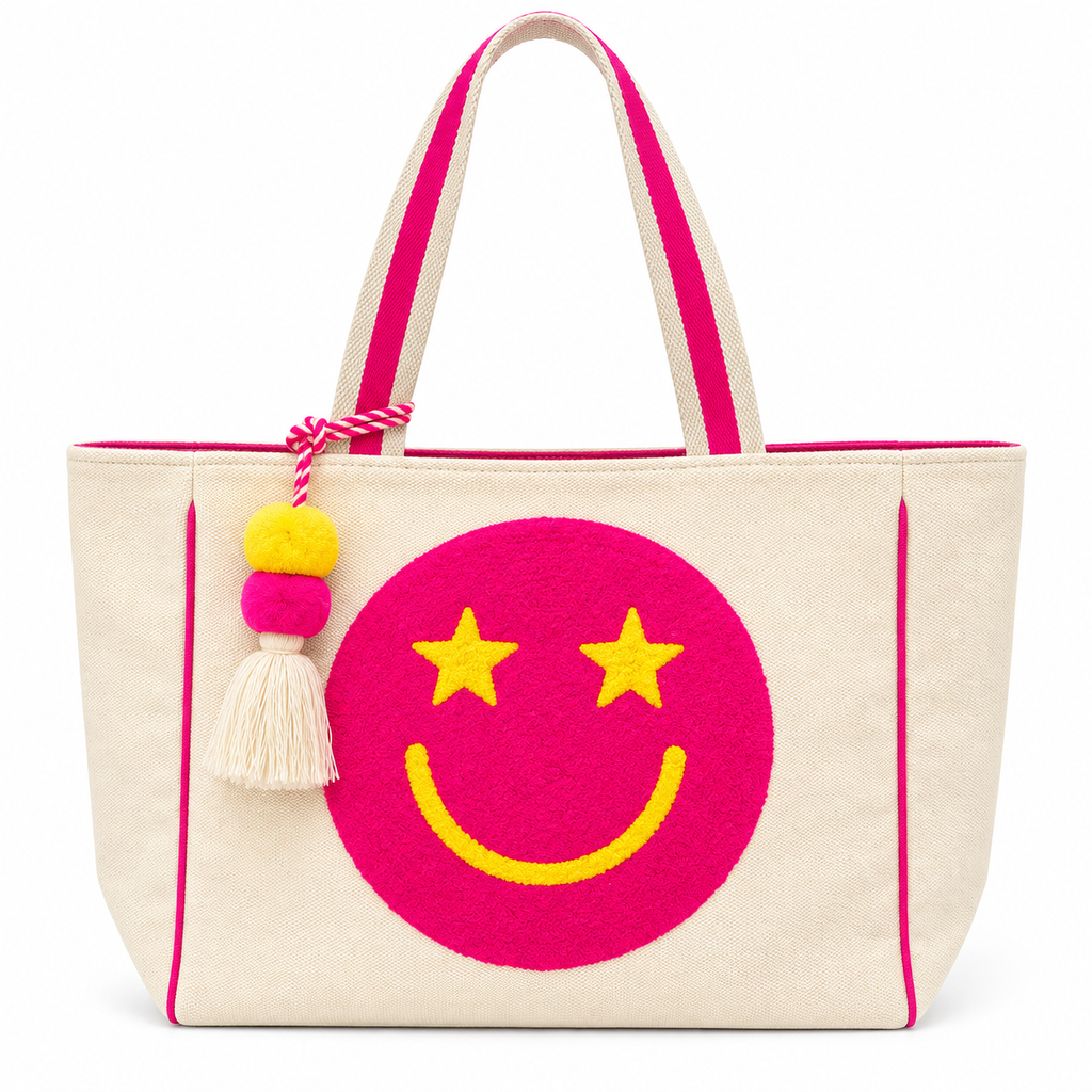 Pink Star Smiley Canvas Tote Bag front view showing natural canvas body with oversized hot pink chenille smiley face patch, yellow star eyes and smile, hot pink trim piping, pink-striped dual shoulder handles, and yellow and pink pom-pom tassel charm with cream fringe on white background
