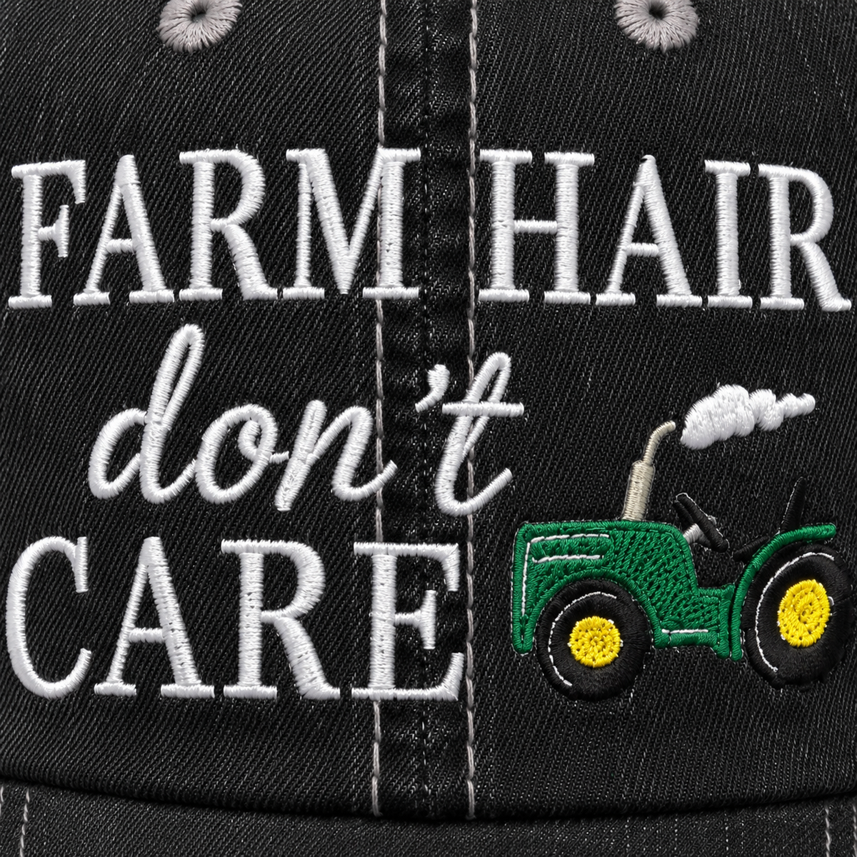 Close-up of embroidered "Farm Hair Don't Care" lettering with green tractor detail on a distressed black trucker hat front panel.
