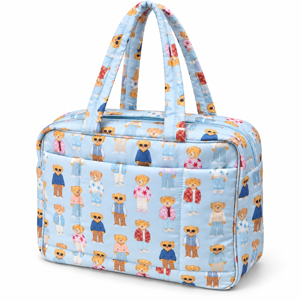 Blue Teddy Bear Weekender Bag three-quarter angle view showing light blue quilted nylon with allover teddy bear print, structured rectangular shape, open front slip pocket, light blue top zipper, and dual padded print handles on white background
