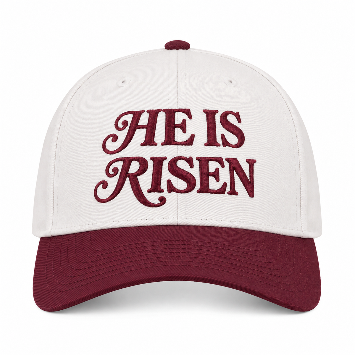 He Is Risen Baseball Cap in Raisin front view showing cream cotton crown with deep burgundy decorative script He Is Risen embroidery, solid raisin bill, and raisin top button on white background
