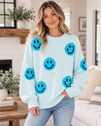 Model wearing the light blue knit happy face sweater with textured turquoise smileys and dark blue facial details with jeans

