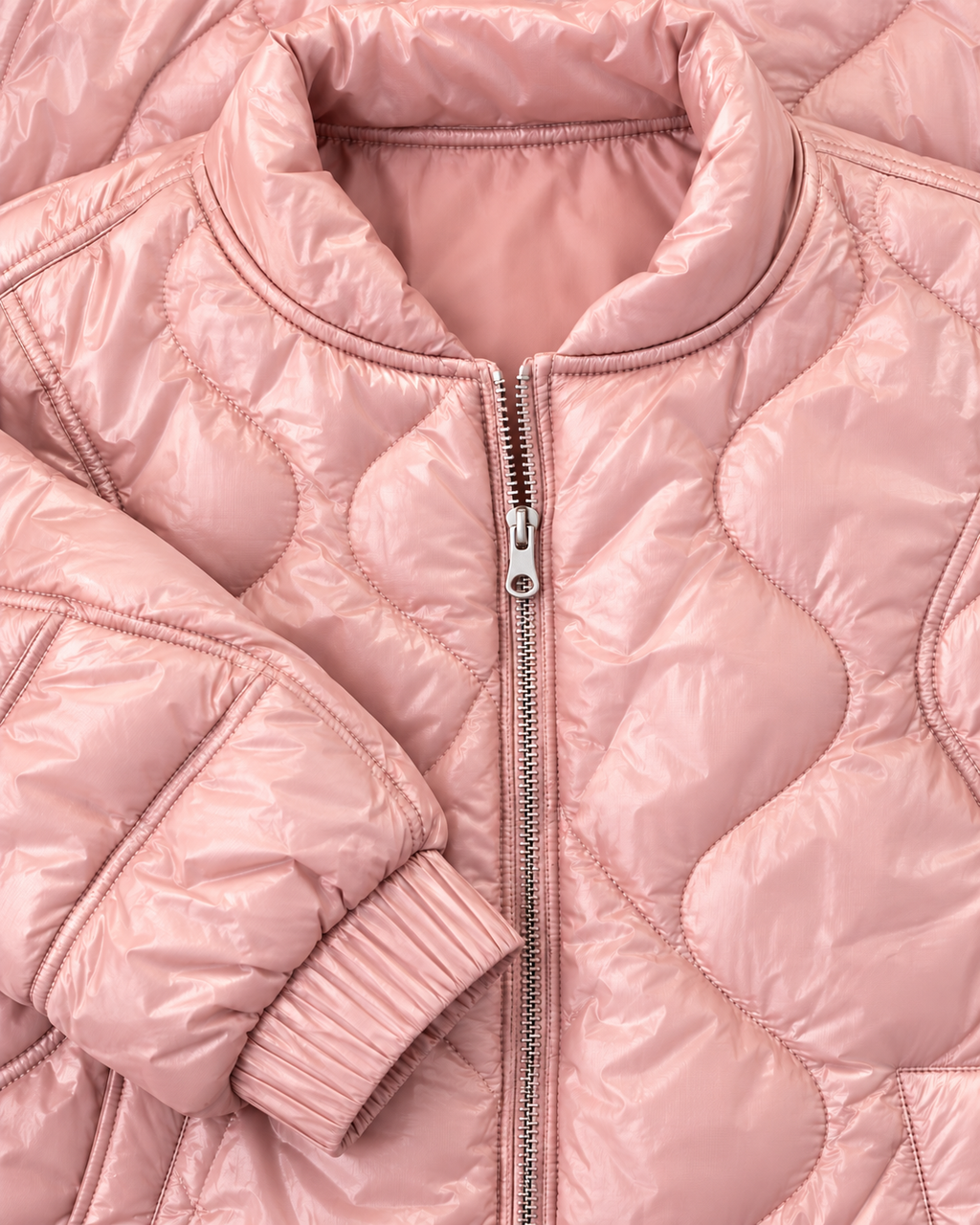 Close-up of the blush pink jacket showing its stand-up collar, silver-tone zipper, curved quilting, and elastic cuff
