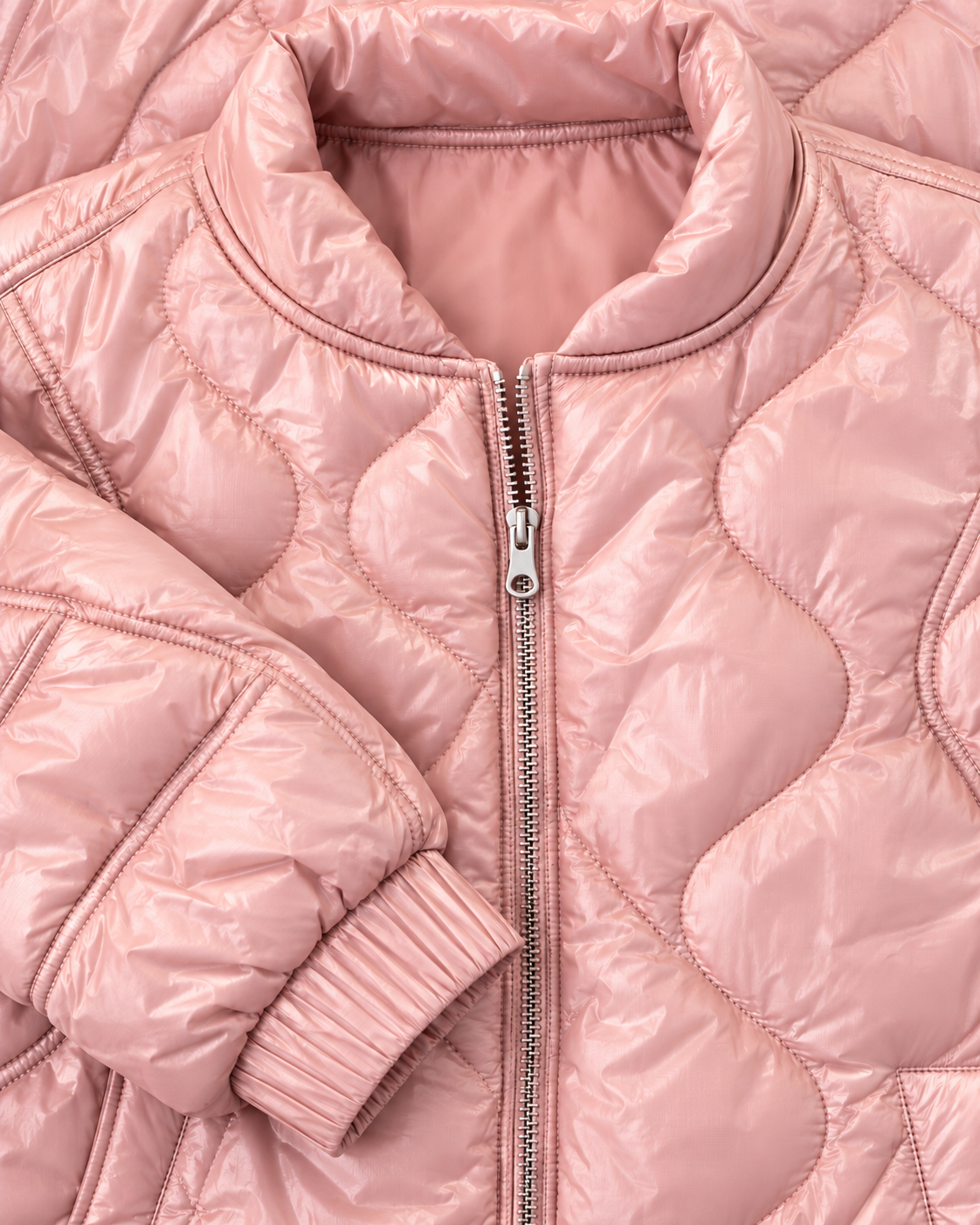 Close-up of the blush pink jacket showing its stand-up collar, silver-tone zipper, curved quilting, and elastic cuff

