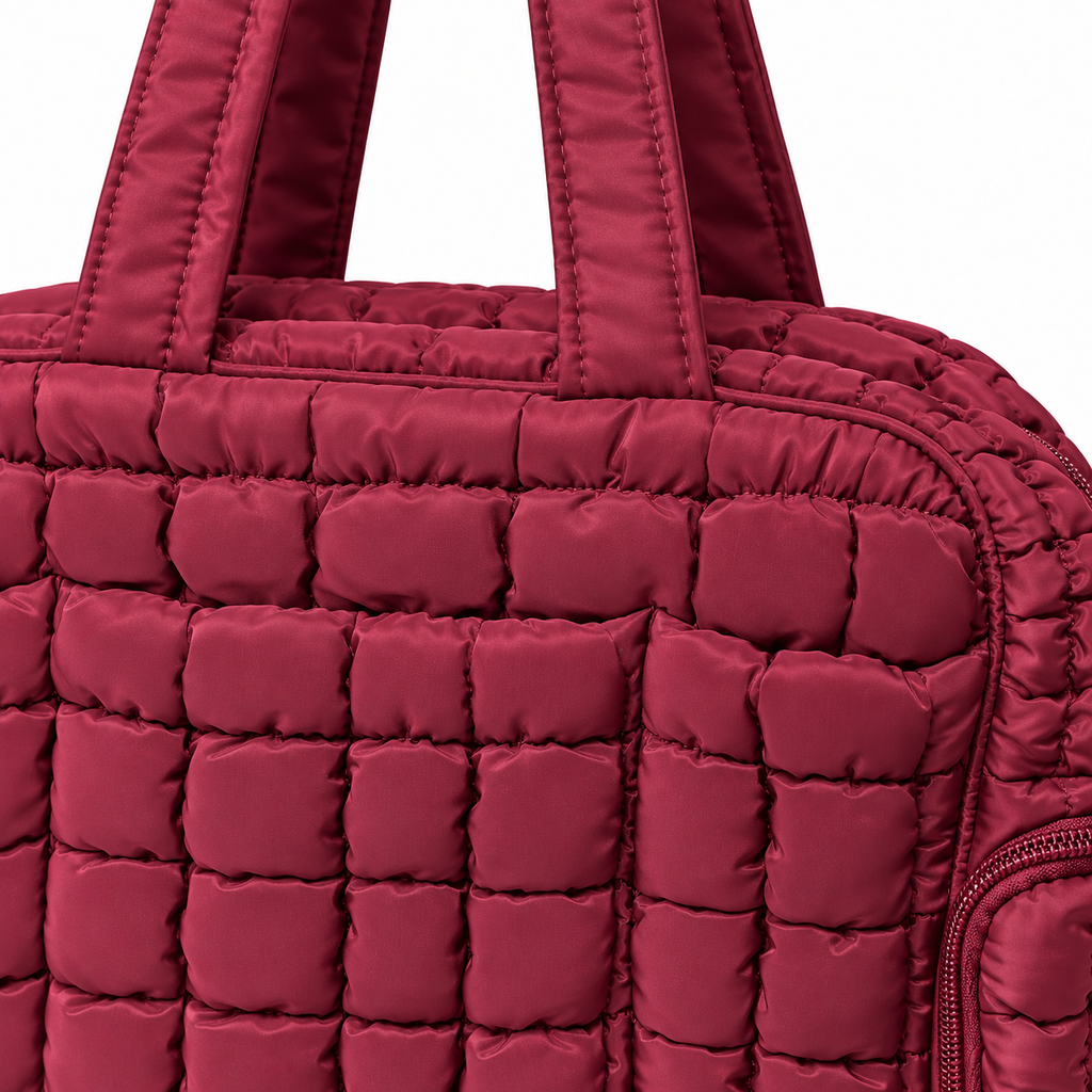 Close-up of Wine Quilted Puffer Tote Bag showing rich wine burgundy puffer nylon grid-quilted texture, dual flat padded shoulder handles with tone-on-tone stitching, zippered top edge, and side zippered pocket
