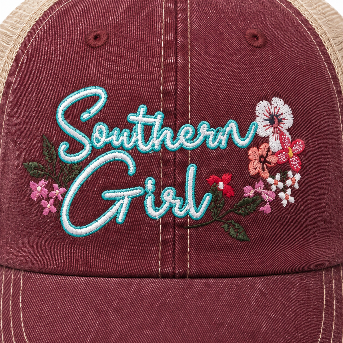 Close-up of Southern Girl trucker hat showing aqua and white embroidered lettering surrounded by detailed pink, red, white, and green floral embroidery.