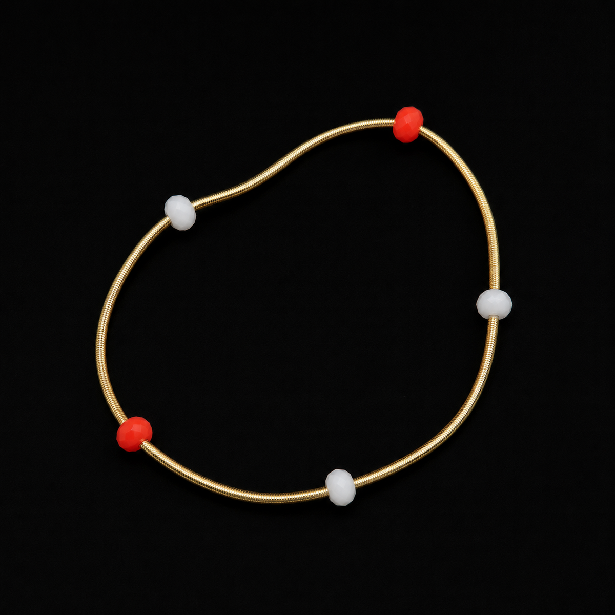 Gold snake coil stretch bracelet with alternating red and white faceted rondelle bead accents displayed flat in a circle on black background
