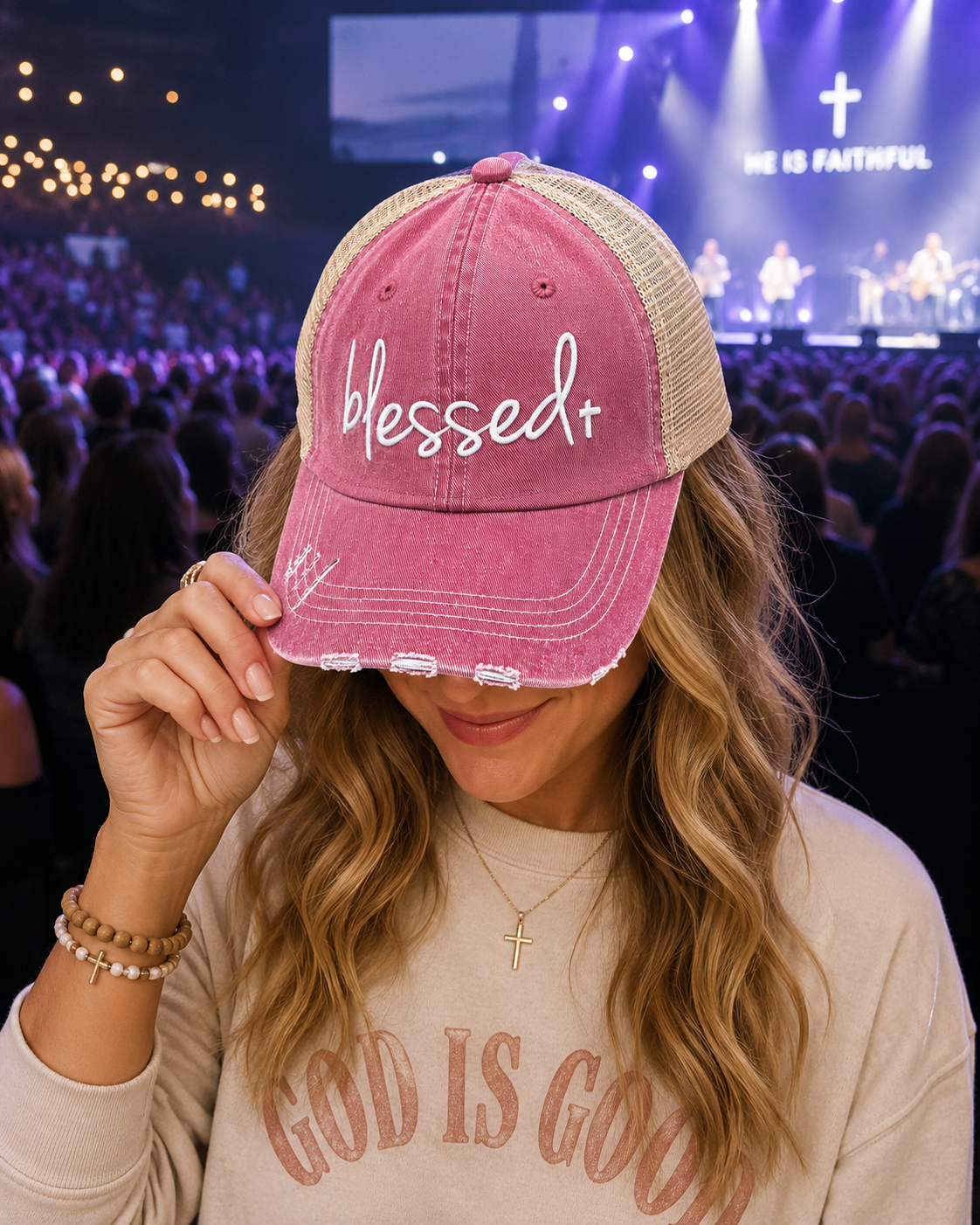 A woman wearing a dusty pink and beige trucker hat with 'Blessed+' embroidered on the front, holding the brim over her eyes.