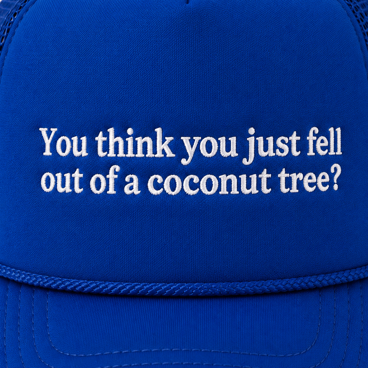 Close-up of white embroidered "You think you just fell out of a coconut tree?" lettering on a royal blue trucker hat foam front panel with rope accent along the brim.
