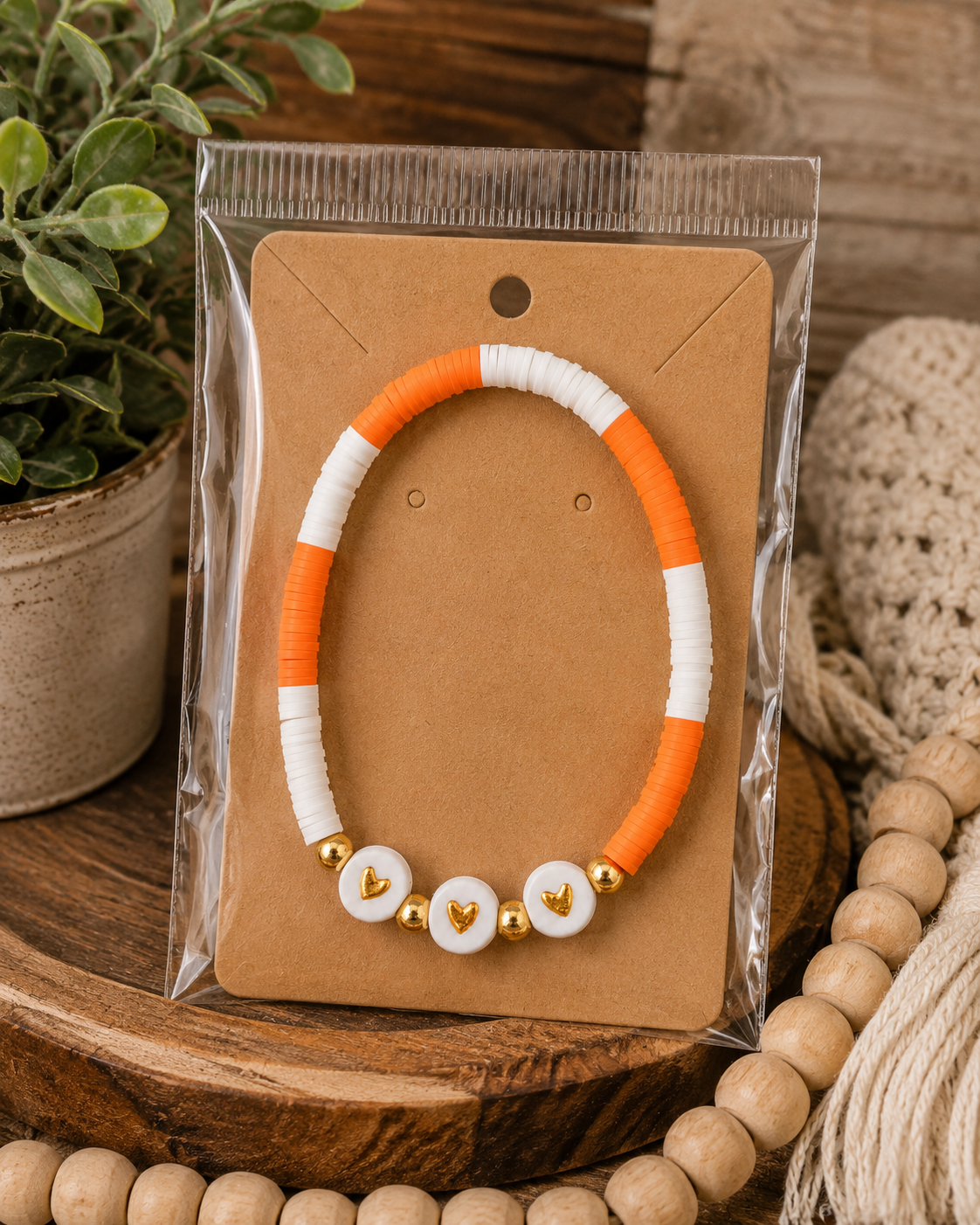 Orange and white heart beaded bracelet on kraft card in clear packaging displayed on wood tray with wood beads
