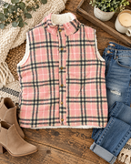Pink plaid fleece-lined vest styled with distressed jeans, tan ankle boots, a textured throw, greenery, and a candle on rustic wood
