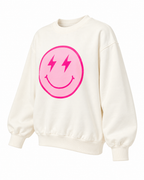Angled front view of the cream lightning-bolt smiley sweatshirt showing its pink graphic, long sleeves, and ribbed trim
