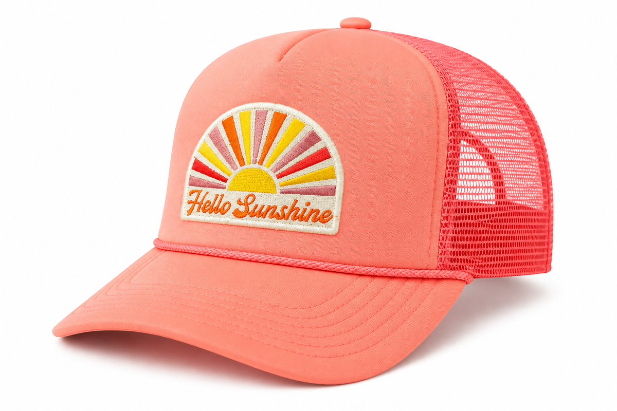Side view of Hello Sunshine trucker hat in coral pink with retro sunburst embroidered patch and mesh back, shown on a white background.
