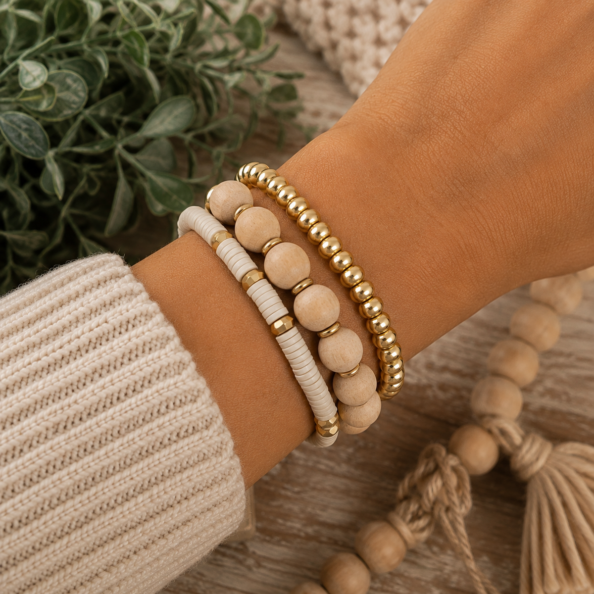 Gold beaded stretch bracelet stacked with two neutral beaded bracelets on wrist with cream sweater

