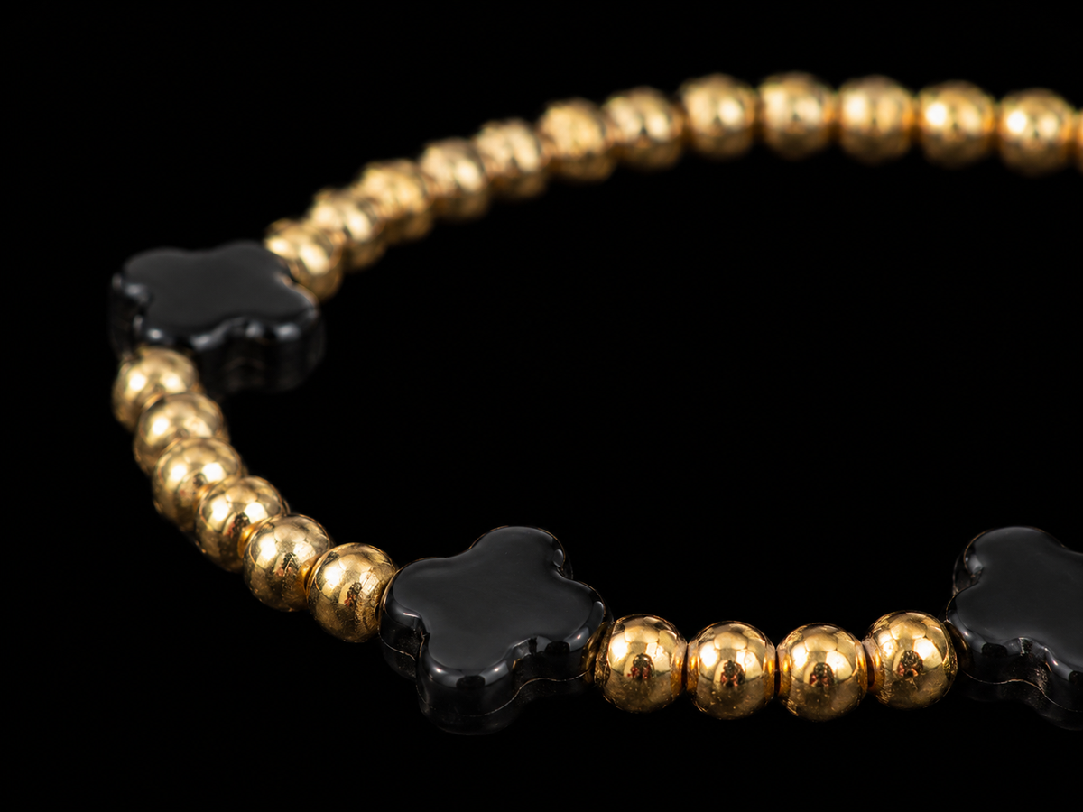 Close-up of matte black clover accent beads flanked by polished gold-tone round beads on stretch bracelet
