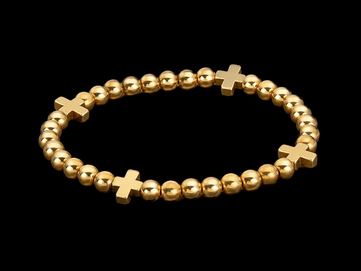 Gold cross beaded stretch bracelet with four evenly spaced gold cross accents shown at an angle on black reflective surface
