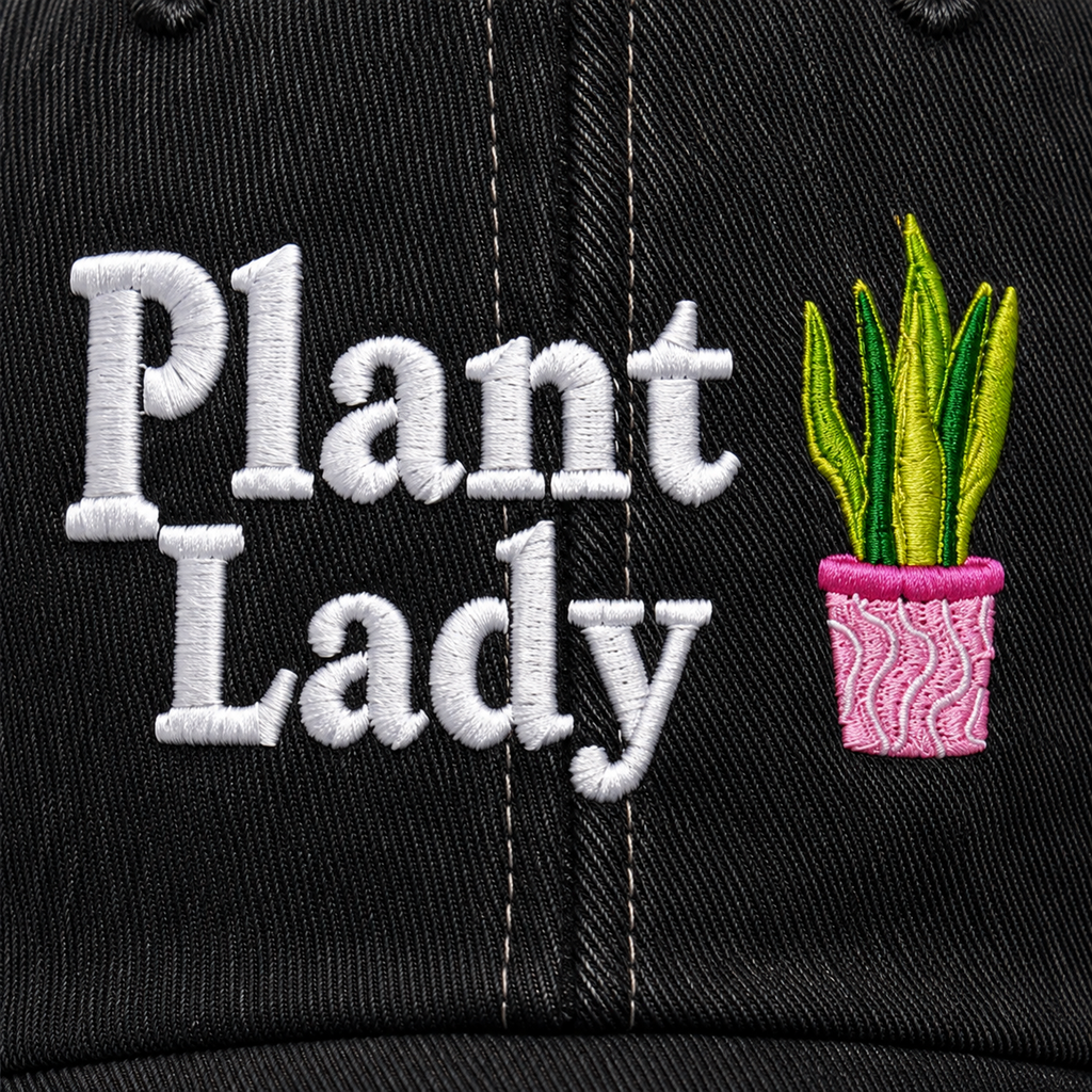 Close-up of embroidered "Plant Lady" lettering with potted snake plant graphic on a washed black trucker hat front panel.
