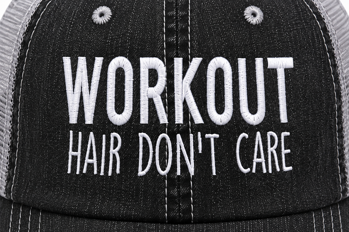 Close-up of white embroidered "Workout Hair Don't Care" lettering on a distressed black trucker hat front panel.
