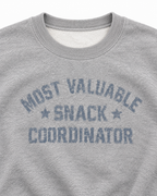 Close-up of distressed Most Valuable Snack Coordinator lettering, star accents, and the ribbed crew neckline
