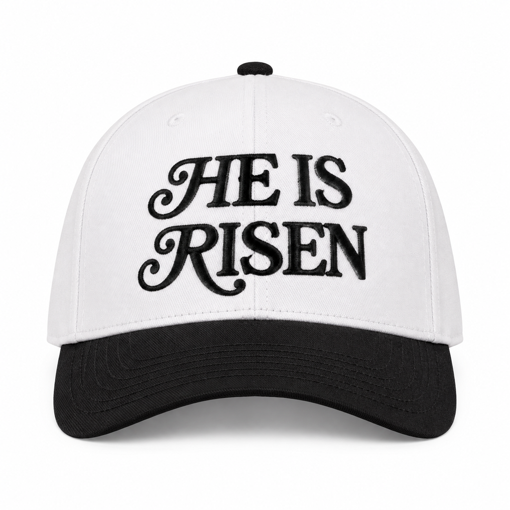 He Is Risen Baseball Cap in Black front view showing white cotton crown with black decorative script He Is Risen embroidery, solid black bill, and black top button on white background
