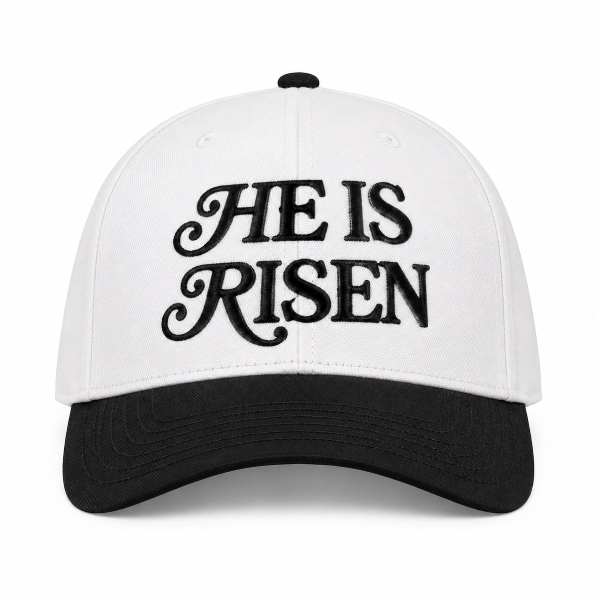 He Is Risen Baseball Cap in Black front view showing white cotton crown with black decorative script He Is Risen embroidery, solid black bill, and black top button on white background
