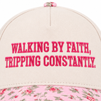 Close-up of Walking By Faith Tripping Constantly Baseball Cap in Floral showing hot pink raised block embroidered lettering reading Walking By Faith Tripping Constantly on cream structured cotton crown with pink floral bill edge visible at bottom on white background
