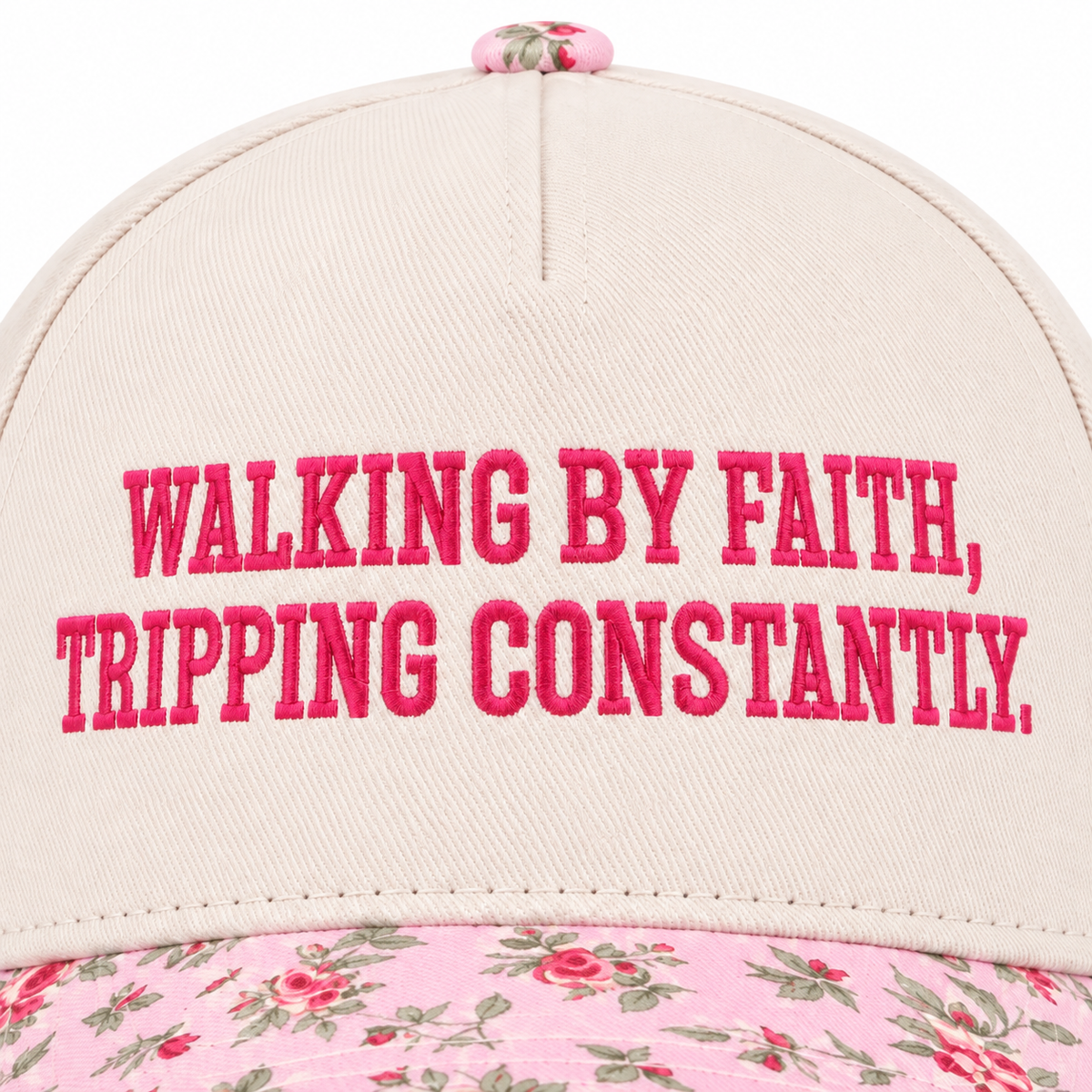 Close-up of Walking By Faith Tripping Constantly Baseball Cap in Floral showing hot pink raised block embroidered lettering reading Walking By Faith Tripping Constantly on cream structured cotton crown with pink floral bill edge visible at bottom on white background
