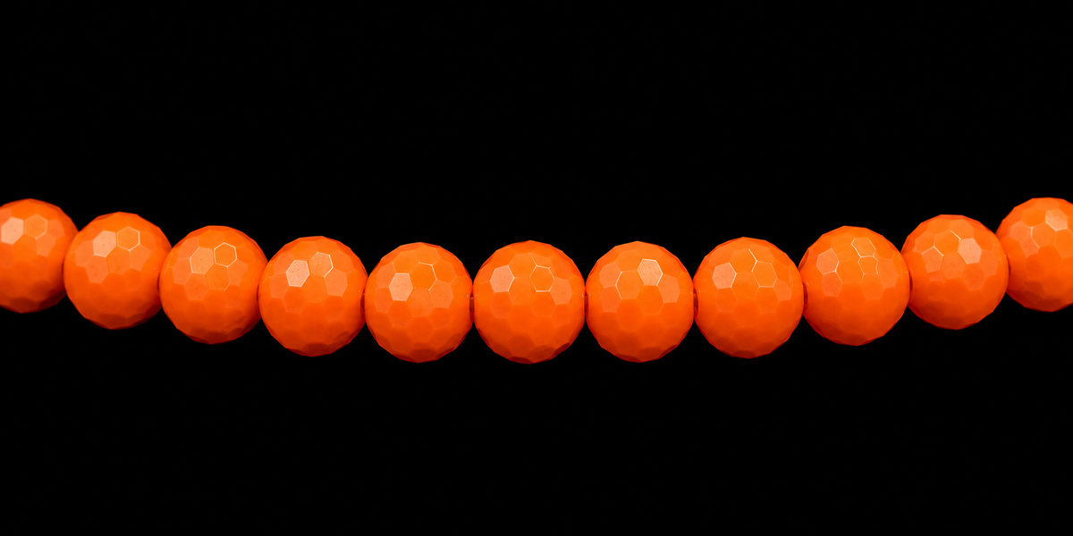 Close-up of neon orange faceted rondelle beads on stretch bracelet against black background
