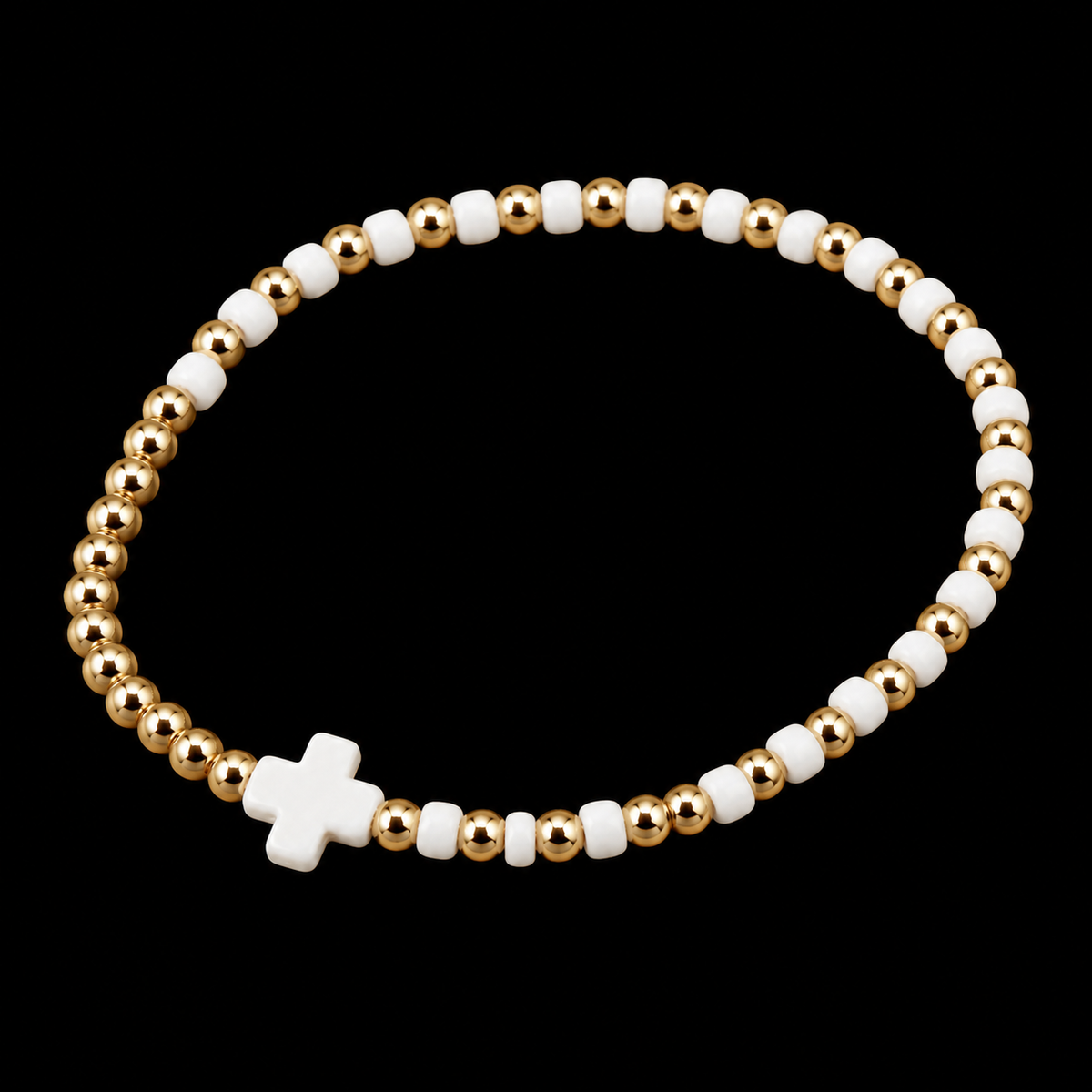 Gold and white cross beaded stretch bracelet shown at an angle on black reflective surface
