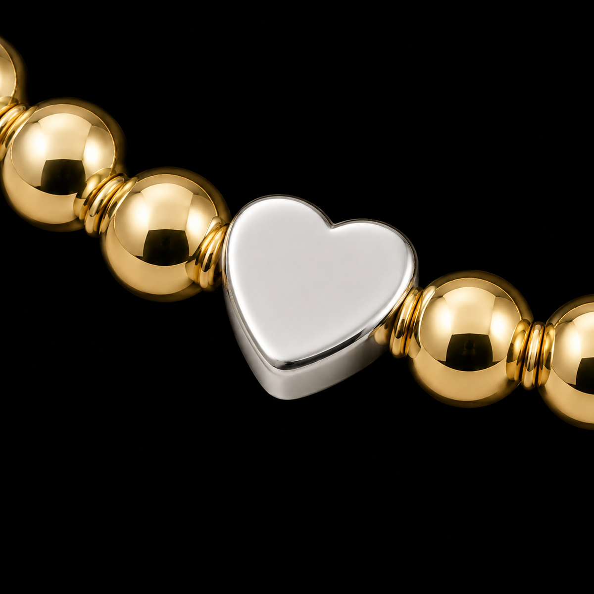Close-up of silver-tone heart accent bead surrounded by polished gold-tone beads on stretch bracelet
