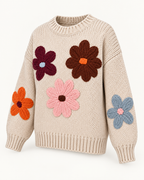 Angled view of the tan floral knit sweater showing colorful stitched flowers across the front and sleeves, dropped shoulders, and ribbed trim
