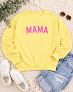 Yellow MAMA sweatshirt styled with blue jeans, white sneakers, sunglasses, and greenery on a cream textured background
