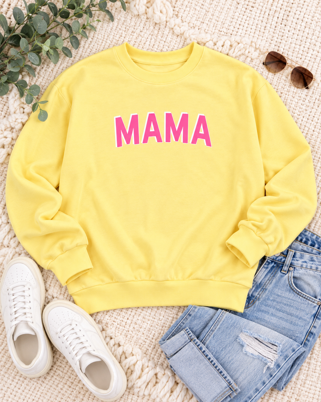 Yellow MAMA sweatshirt styled with blue jeans, white sneakers, sunglasses, and greenery on a cream textured background
