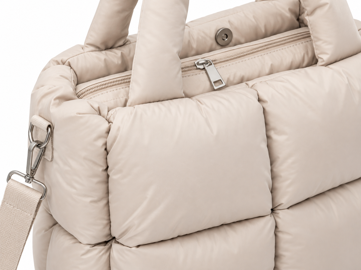 Close-up of Sand Mini Quilted Puffer Tote showing top zipper closure with silver zipper pull, snap button detail, padded rounded handles, and soft sand neutral puffer quilted panel construction
