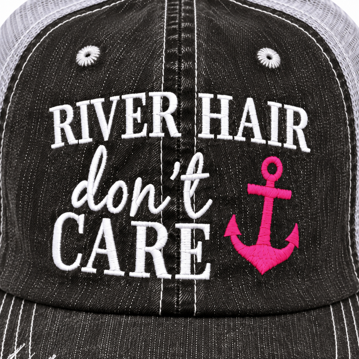 Close-up of white embroidered River Hair block lettering, don't script lettering, and Care block lettering with hot pink embroidered anchor on distressed black trucker hat front panel
