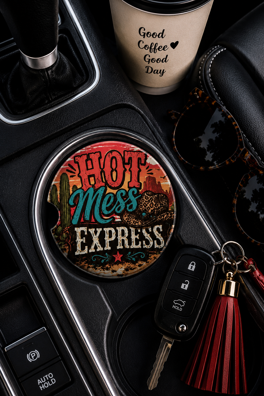
Hot Mess Express ceramic car coaster sitting in a vehicle cup holder, styled with car keys, sunglasses, and a coffee cup — retro western desert design with cactus and leopard print
