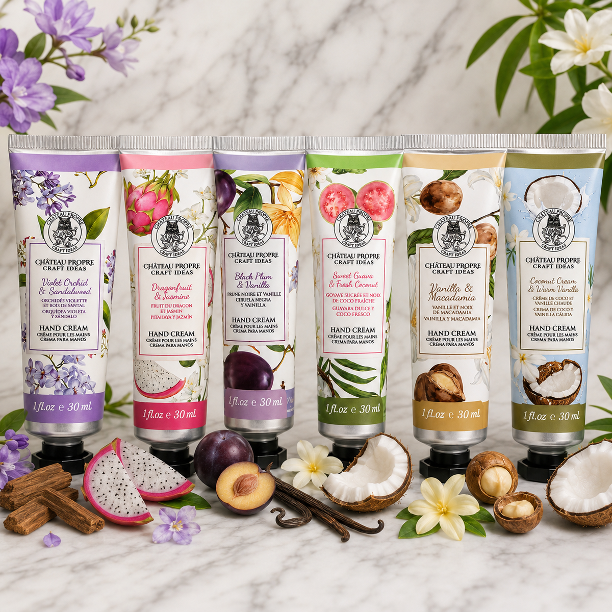 Six tubes of Château Propre Craft Ideas hand cream arranged on a marble surface with tropical fruits, flowers, and vanilla beans, featuring scents including Dragonfruit, Black Plum, Vanilla, and Coconut.
