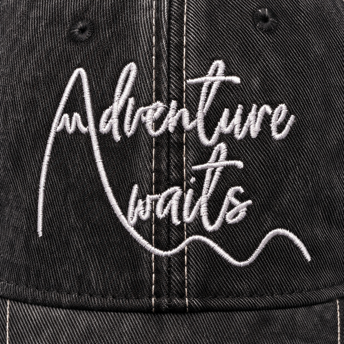 Close-up of white Adventure Awaits script embroidery on distressed black trucker hat
