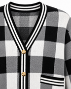 Close-up of Black and White Plaid Gold Button Knit Cardigan showing deep V-neckline with black and white striped knit trim, antique gold dome buttons along placket, and striped patch pocket trim on black and white plaid knit on white background
