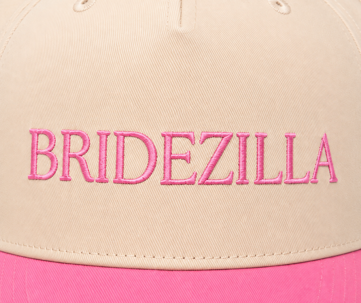 Side view of Bridezilla Baseball Cap showing cream structured crown, hot pink brim, and solid back, on a white background.
