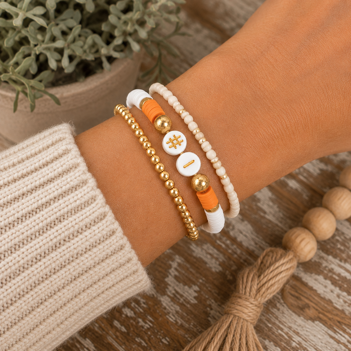 Orange and white #1 beaded bracelet stacked with gold beaded and cream seed bead bracelets on wrist with cream sweater
