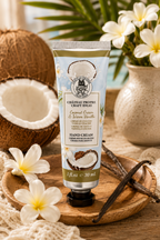 A tube of Château Propre Craft Ideas Coconut Cream & Warm Vanilla Hand Cream stands on a wooden tray, surrounded by tropical props including a halved coconut, vanilla beans, and white flowers.