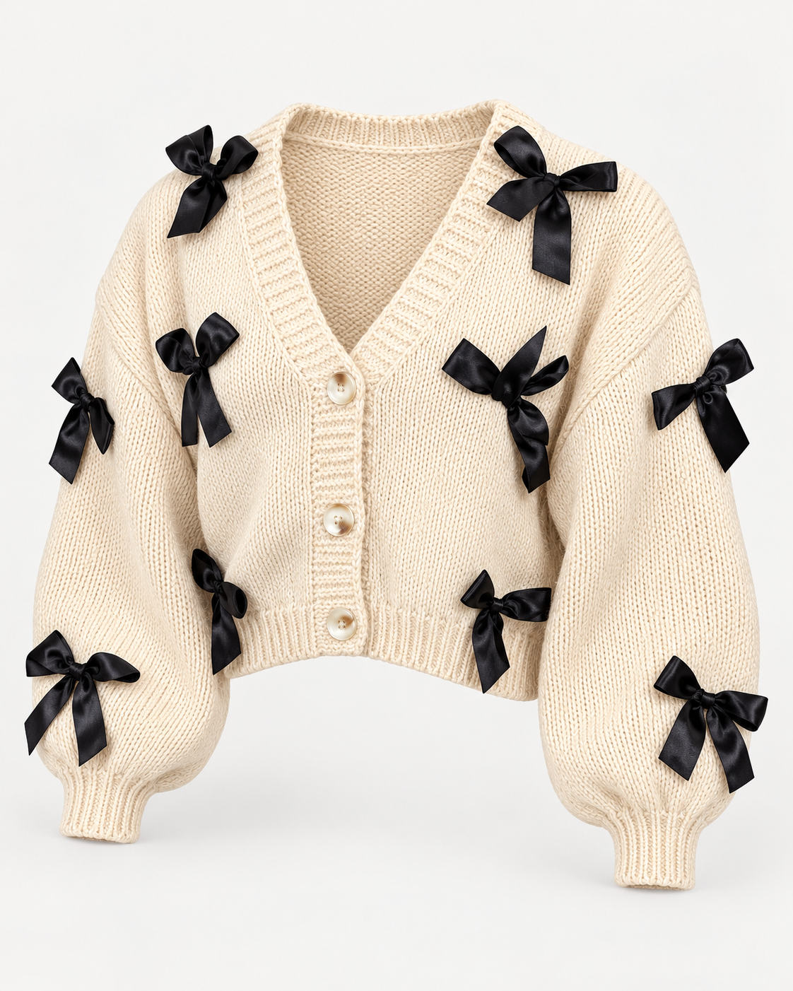 Angled view of the tan knit cardigan showing black bows across the front and sleeves, dropped shoulders, ribbed cuffs, and cropped hem
