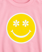Close-up of the yellow happy face graphic with white daisy-shaped eyes, a white smile, and a white border on pink fabric
