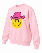 Angled front view of the light pink cowgirl smiley sweatshirt showing its cowboy hat graphic, long sleeves, and ribbed trim
