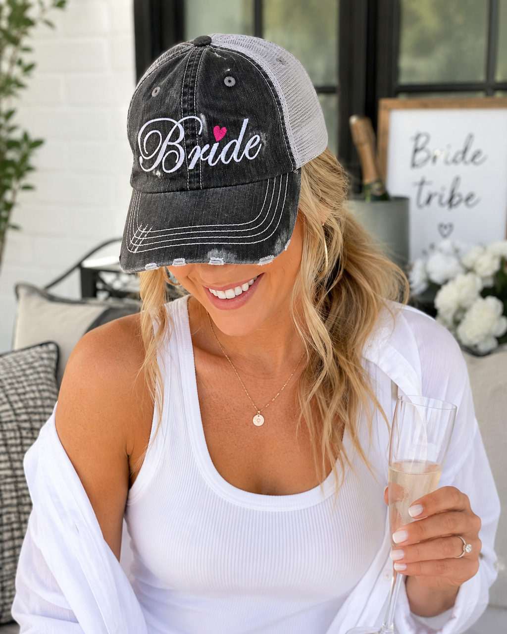 Woman wearing Bride distressed charcoal trucker hat while holding champagne glass at bridal celebration
