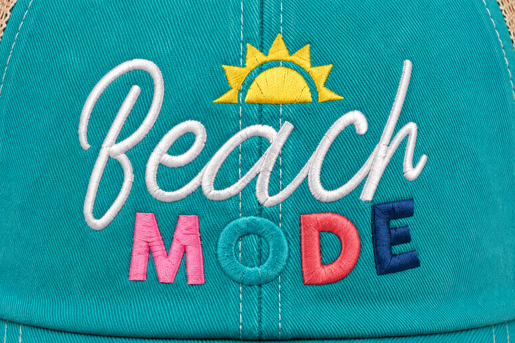 Close-up of colorful "Beach Mode" embroidered patch on a teal distressed trucker hat front panel.
