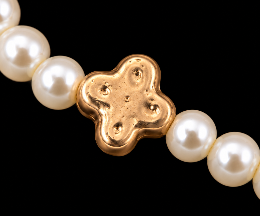 Close-up of creamy white pearl bead and hammered gold-tone clover accent bead on stretch bracelet
