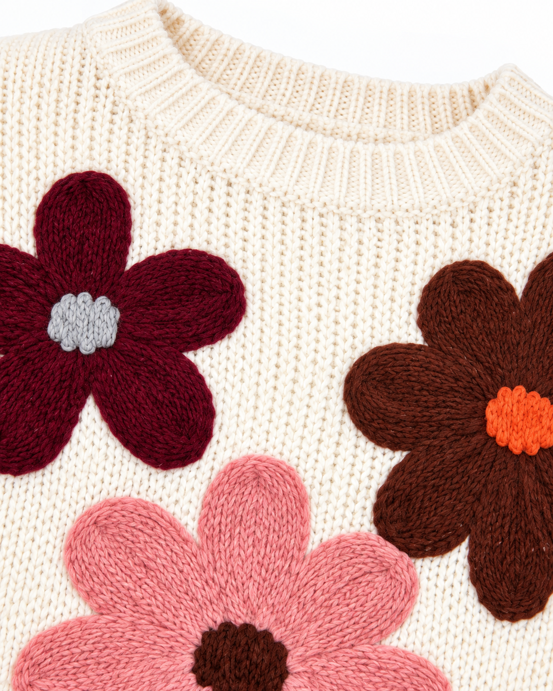 Close-up of Cream Floral Knit Stitched Sweater showing ribbed crew neckline and three oversized 3D knit daisy appliqués in burgundy with gray center, brown with orange center, and pink with brown center on cream ribbed knit
