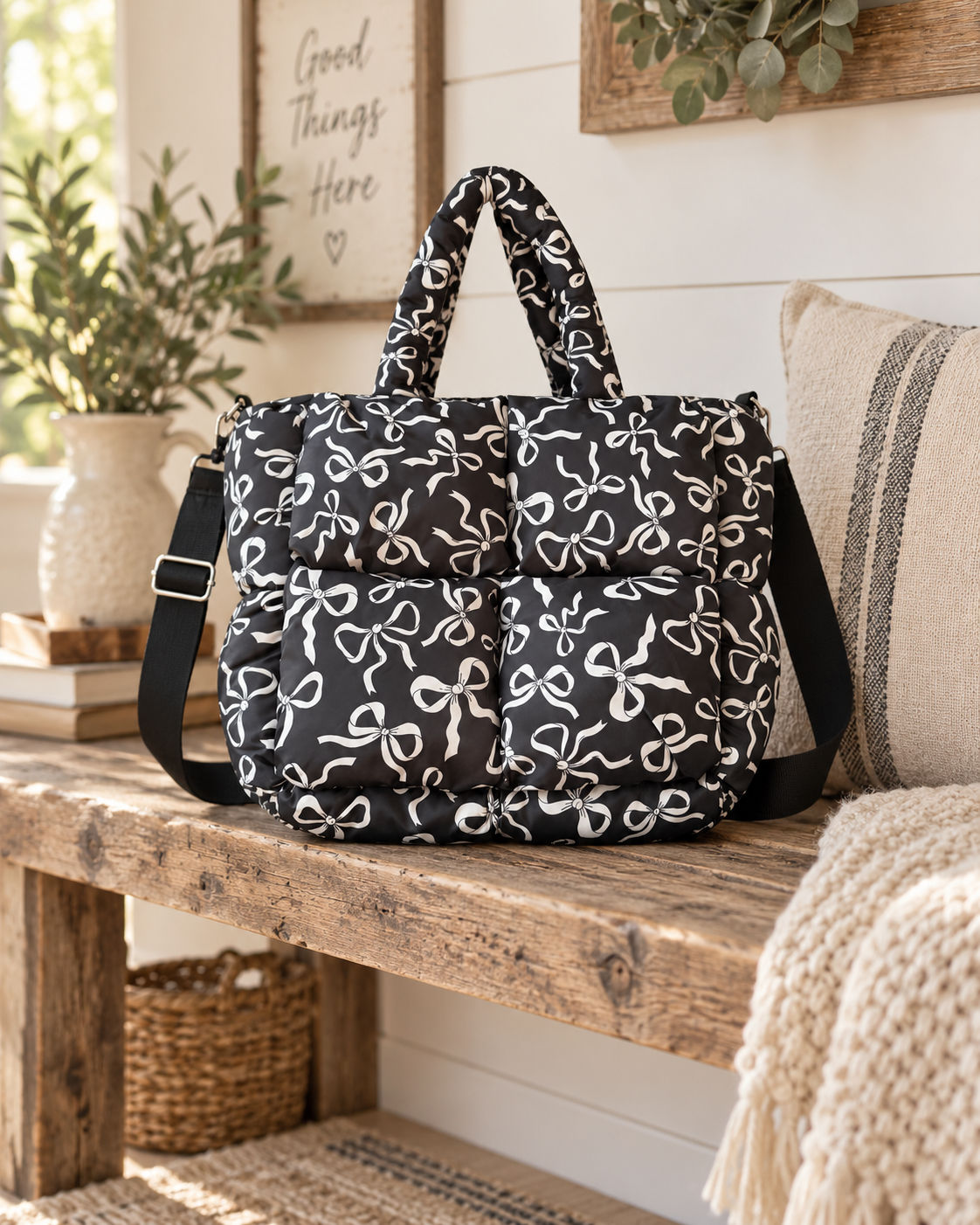 Black Bow Print Puffer Tote displayed on rustic wooden bench showing black puffer body with all-over white bow print, dual top handles, and adjustable black crossbody strap with shiplap wall, eucalyptus, and knit throw farmhouse backdrop
